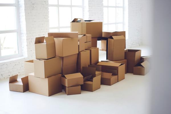 A large pile of boxes stacked up one on top of the other in a white room with a wall of windows.