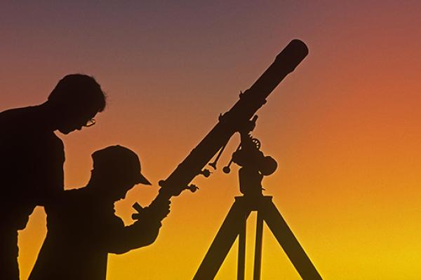 Silhouette of man and young boy with telescope