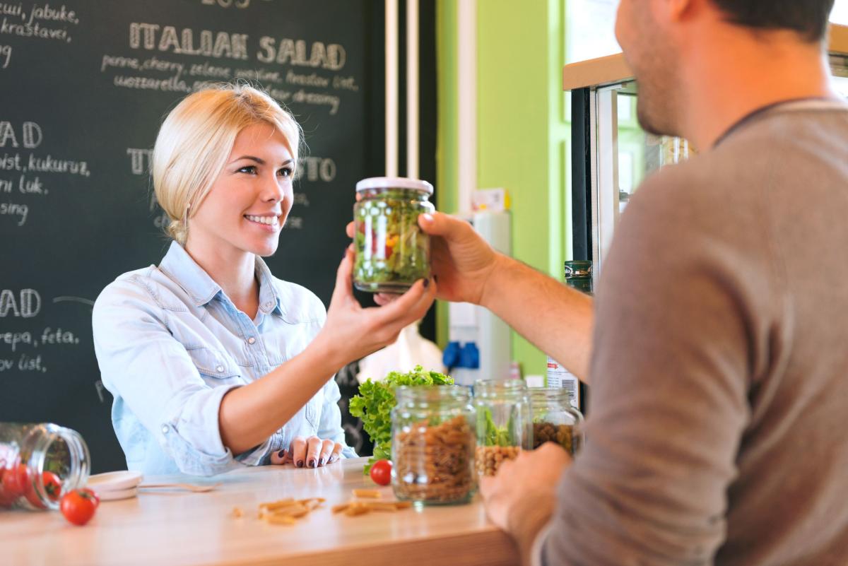 A customer hands a jar of pickles to a staff member at the front counter of a cafe