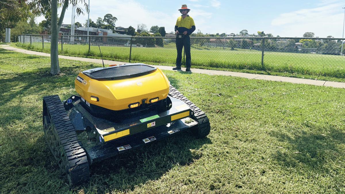 photo of the remote lawn mower being operated by a council officer in the background