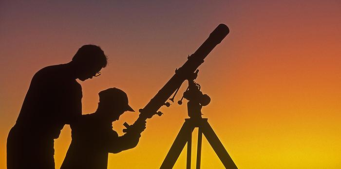 Silhouette of man and young boy with telescope