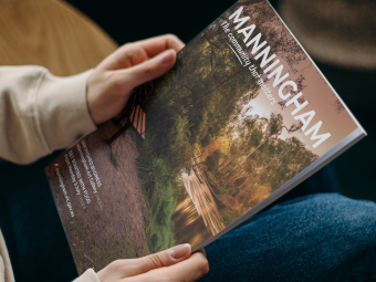 A pair of hands holding a magazine with a beautiful riverside landscape on the cover and the words 'Manningham. The community that matters.'