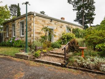 A restored sandstone building in a cottage garden setting. A small sign with the word 'entry' sits at the base of a path leading to the side door of the building.