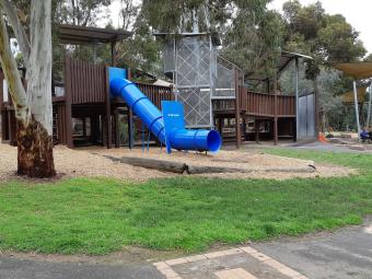 Timber playground structure with blue tunnel slide in bushy parklands