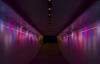 Red, purple and blue waves of light run vertically along the length of a dark underpass, a strip of small white circular lights runs along the ceiling