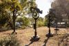 Four tall totemic steel sculptures sit in a clearing amongst bushy native trees, a carpark is in the background.